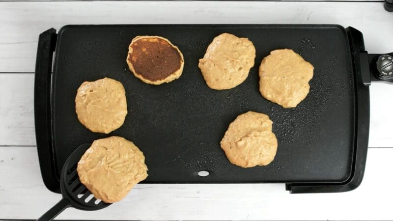 Protein powder pancakes being flipped on griddle.