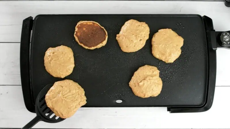 Protein powder pancakes being flipped on griddle.