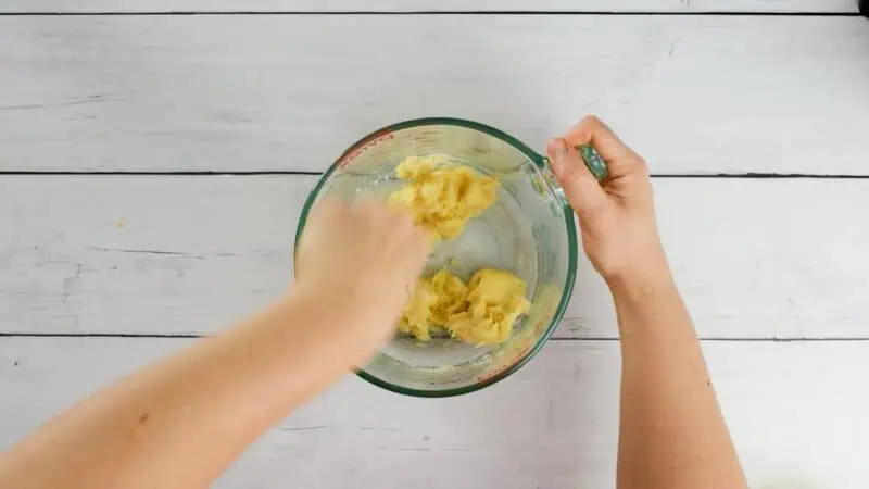 Fork mashing bananas in glass bowl.
