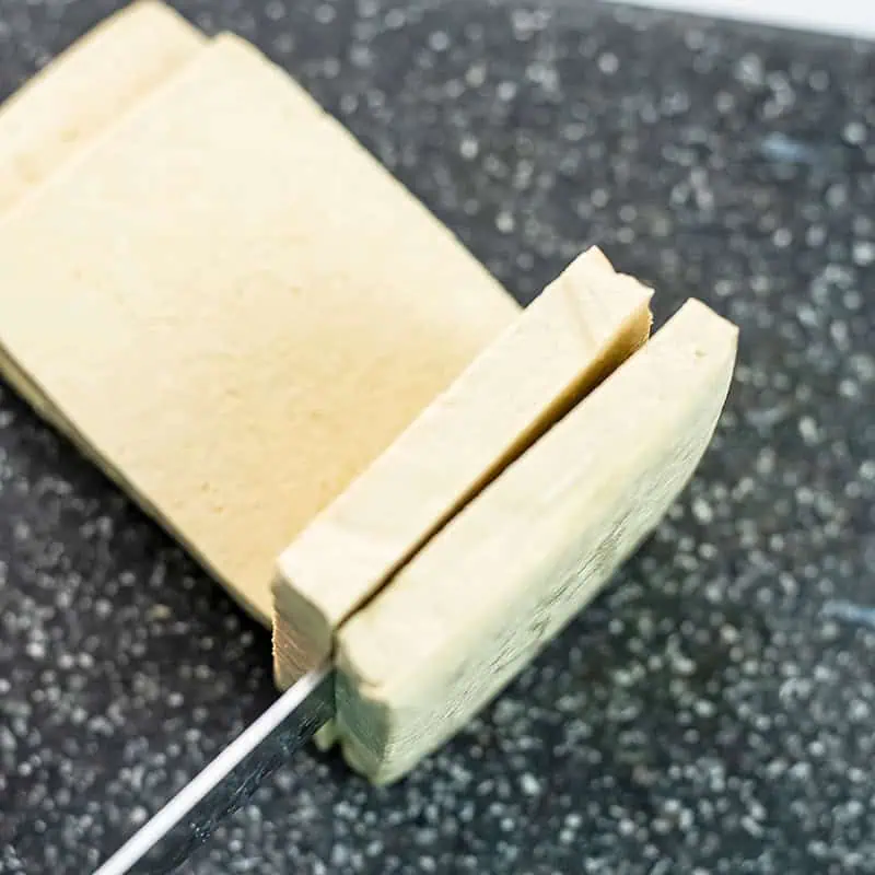 Knife slicing through a block of extra firm tofu. 