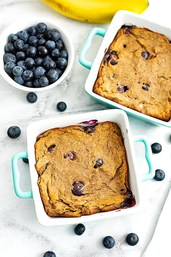 Two square baking dishes filled with blueberry banana bread. blueberries in background