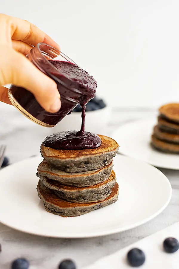 Stack of four pancakes with blueberry syrup being poured over top