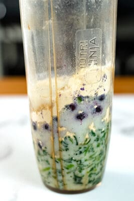 Blueberry spinach smoothie ingredients in a blender cup before being blended.
