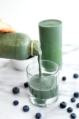 Blueberry spinach smoothie being poured into a small glass.