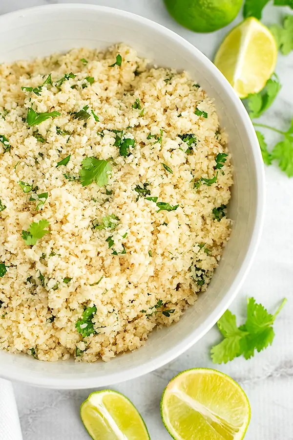 Large bowl of cilantro lime cauliflower rice with cut limes around the bowl.