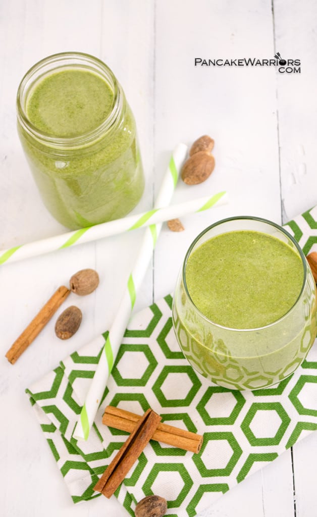 Pumpkin spice green smoothies in two glasses with cinnamon sticks and nutmeg over a green pattern napkin