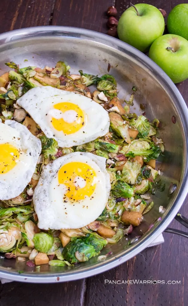 Apple Brussels Sprouts Hash in a skillet with 3 eggs on top.