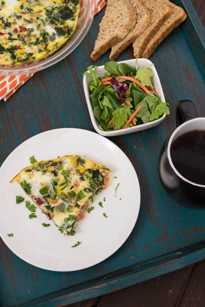 Smoked salmon frittata on a white plate with small salad in background.