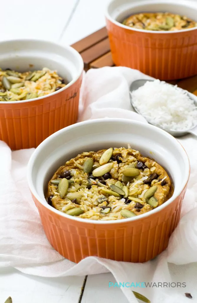 Three simple individual crustless chocolate chip pumpkin pie in orange ramekins on a white napkin and a large spoon of coconut flakes in the background 