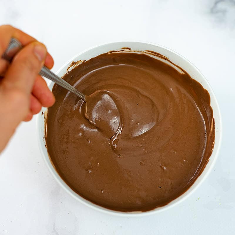 Hand holding spoon, stirring the chocolate protein pudding.