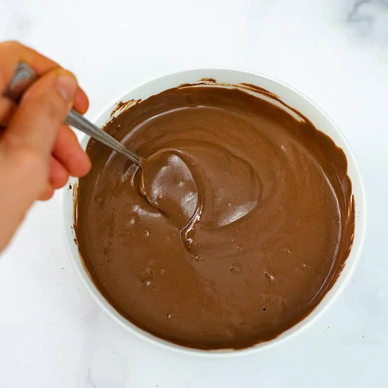 Hand holding spoon, stirring the chocolate protein pudding.
