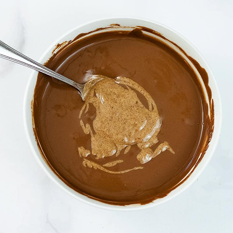 Almond butter added to protein pudding base in white bowl.