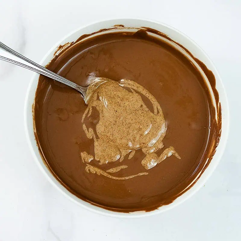 Almond butter added to protein pudding base in white bowl.