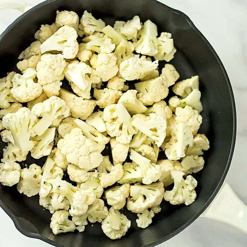 Raw cauliflower florets in a skillet.