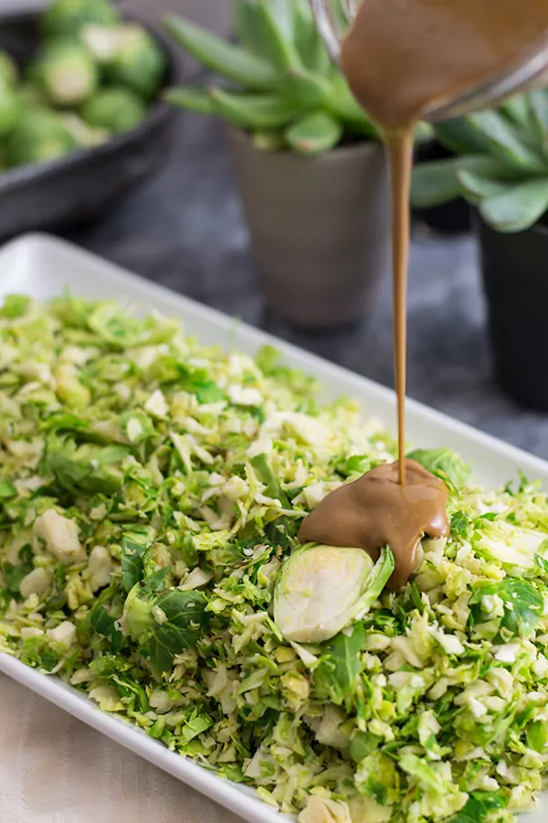 Balsamic dressing being poured on shaved brussels sprouts salad