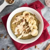 White bowl of gingerbread mug cake over a red napkin topped with sliced bananas, chopped pecans and coconut butter drizzle