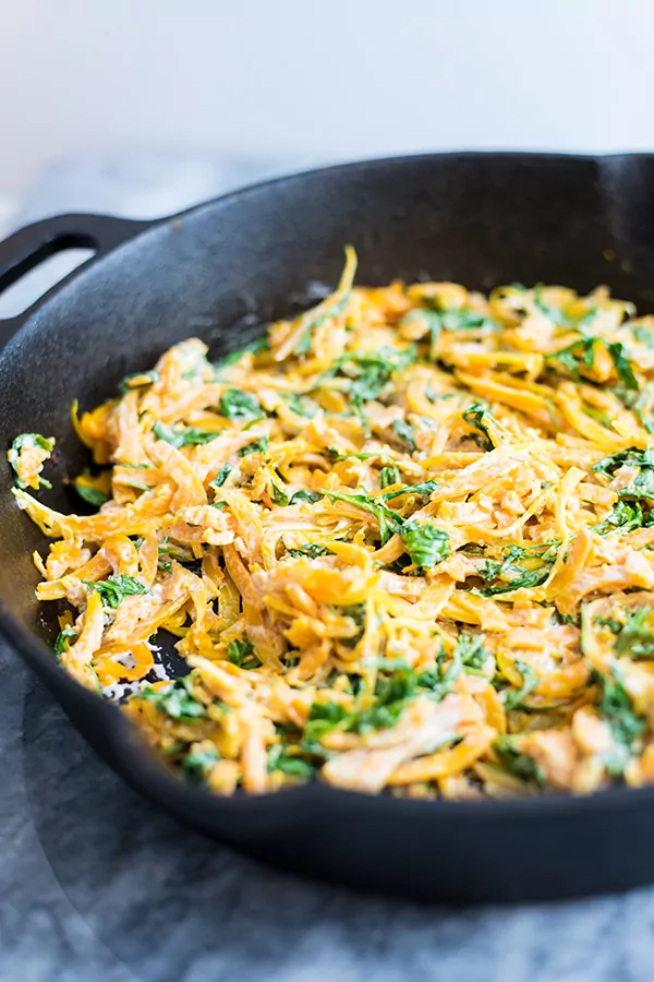butternut squash noodles with a creamy garlic sauce with arugula in a cast iron skillet