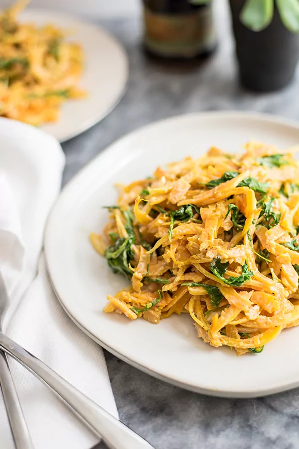butternut squash noodles with a creamy garlic sauce with arugula on white plate with fork