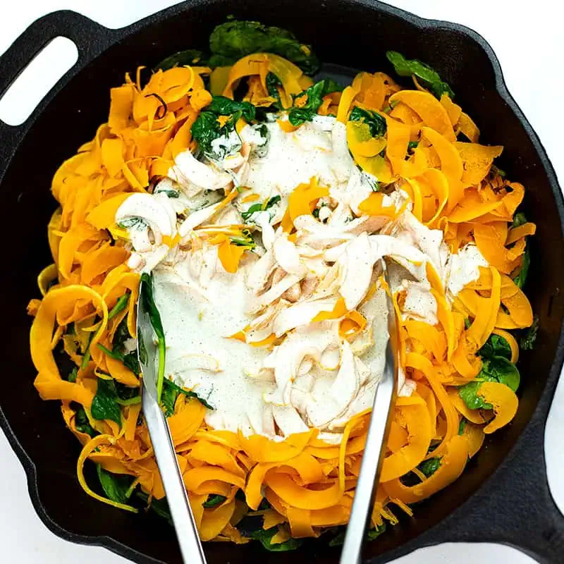 Butternut squash pasta with creamy garlic sauce added in cast iron skillet.