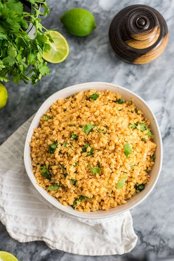 Whole30 Mexican cauliflower rice made with cauliflower rice topped with cilantro over a white lined napkin with limes and cilantro in the background.