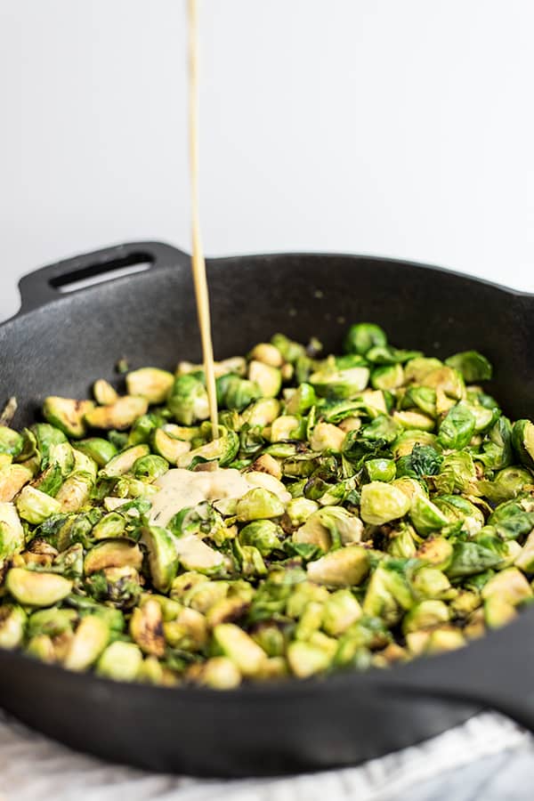 Paleo brussels sprouts in an iron skillet with creamy dijon sauce being poured on it