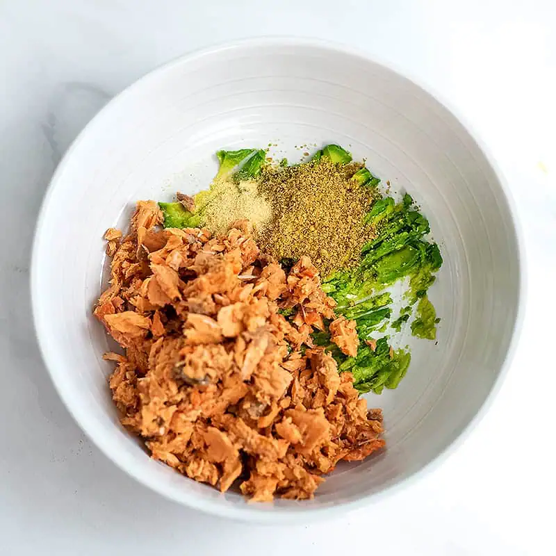 Canned salmon added to bowl with avocado and spices.