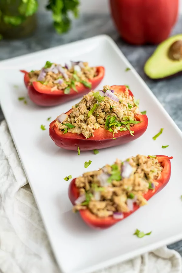 Tuna Stuffed Peppers on a white serving tray with avocado, red bell pepper and cilantro