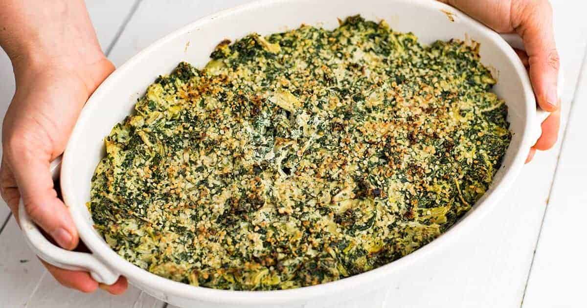 Hands holding Spinach Artichoke Dip in a white casserole dish 