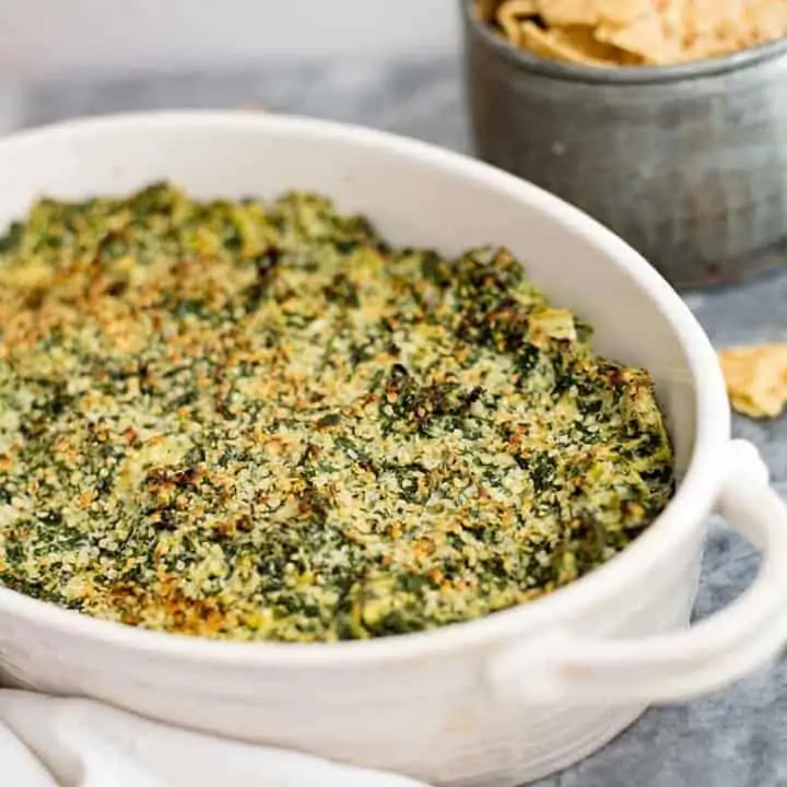 Spinach Artichoke Dip in a white casserole dish with chips