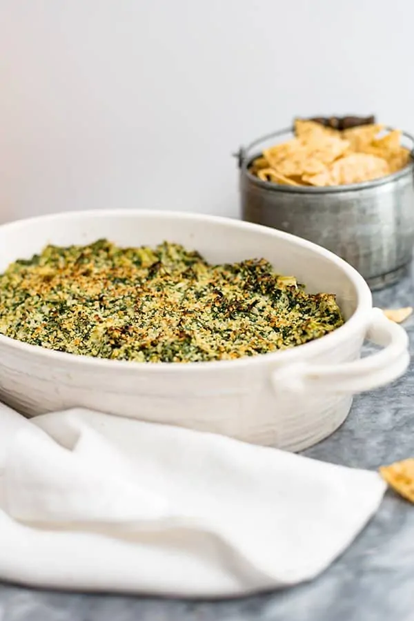Spinach Artichoke Dip in a white casserole dish with chips and white napkin