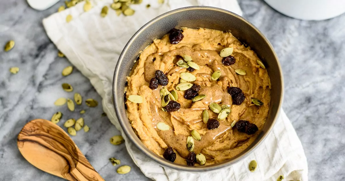 Sweet Potato Breakfast bowl topped with raisins, pumpkin seeds and almond butter in a grey bowl on a white napkin