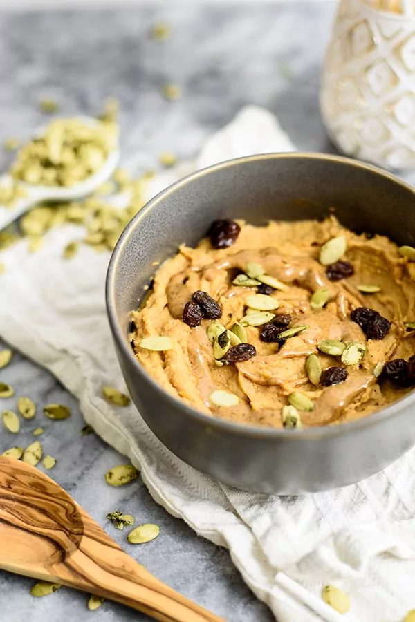 Sweet Potato Breakfast bowl topped with raisins, pumpkin seeds and almond butter in a grey bowl on a white napkin