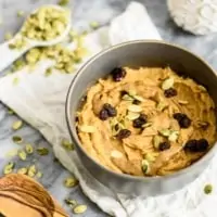 Sweet Potato Breakfast bowl topped with raisins, pumpkin seeds and almond butter in a grey bowl on a white napkin