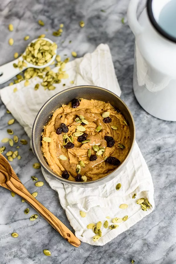 Sweet Potato Breakfast bowl topped with raisins, pumpkin seeds and almond butter in a grey bowl on a white napkin