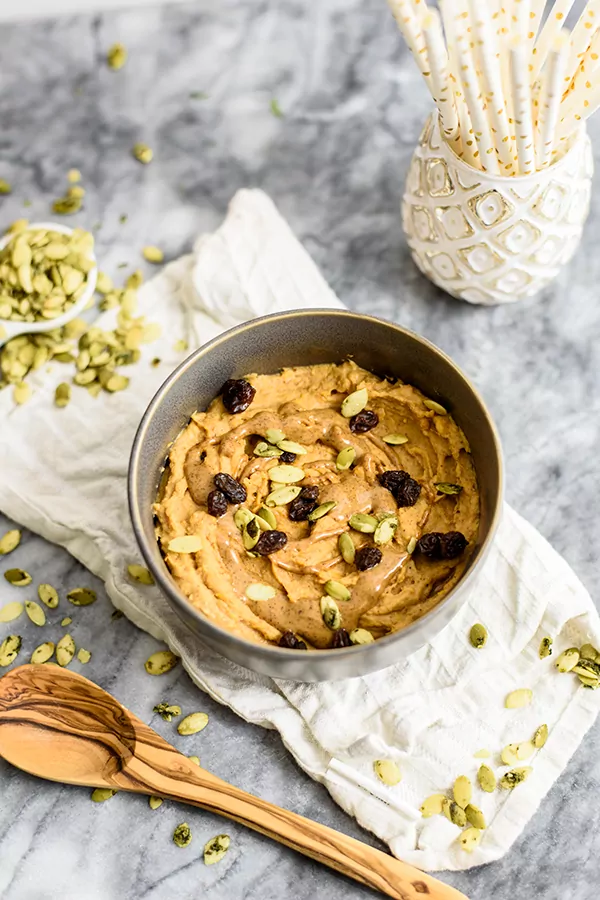 Sweet Potato Breakfast bowl topped with raisins, pumpkin seeds and almond butter in a grey bowl on a white napkin