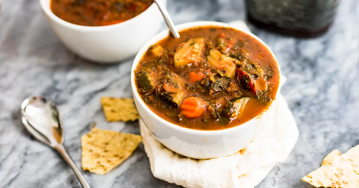 Mediterranean Vegetable Soup in a white bowl with spoon in bowl of soup on white napkin