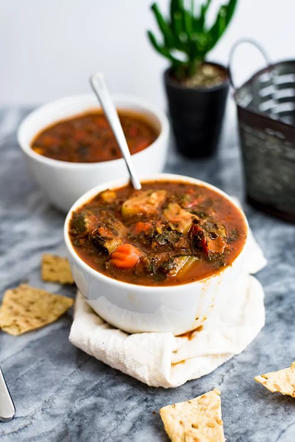 Mediterranean Vegetable Soup in a white bowl with spoon in bowl of soup. 