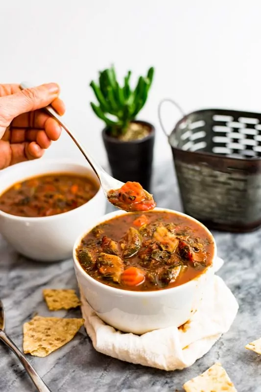 Mediterranean Vegetable Soup in a white bowl with spoon of soup overhead