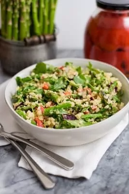 White bowl filled with asparagus spring salad with asparagus and roasted red pepper in background