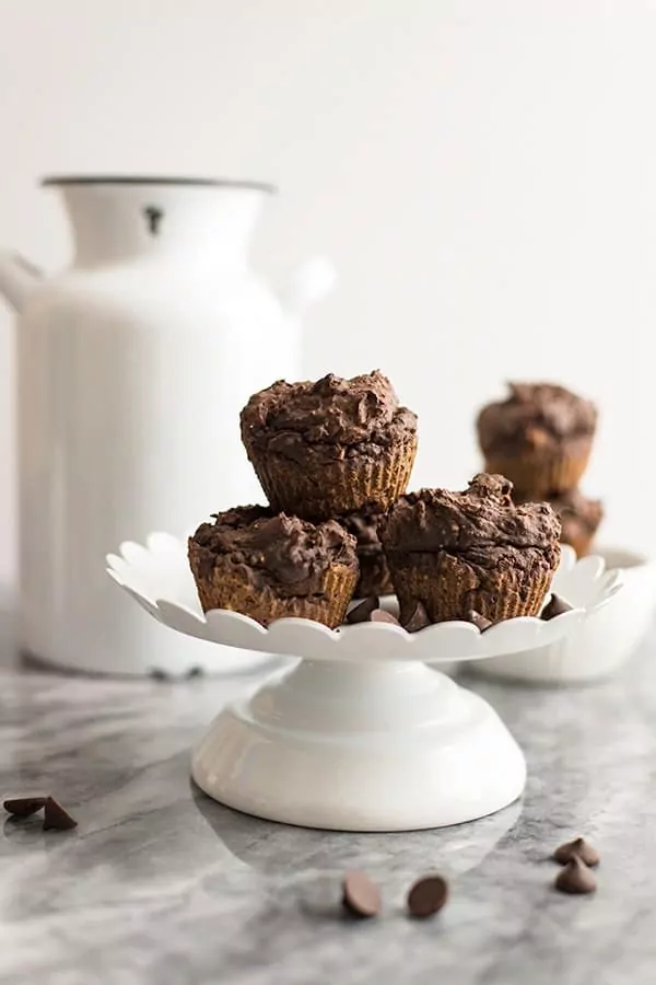 Vegan Chocolate Protein Muffins stacked on a white cake stand with a white jar in the background