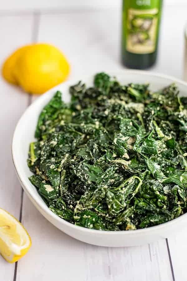 White bowl of creamy kale with a lemon in the background