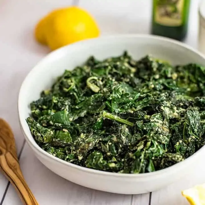 Large bowl of creamy kale with a juiced lemon and a bottle of olive oil in the background