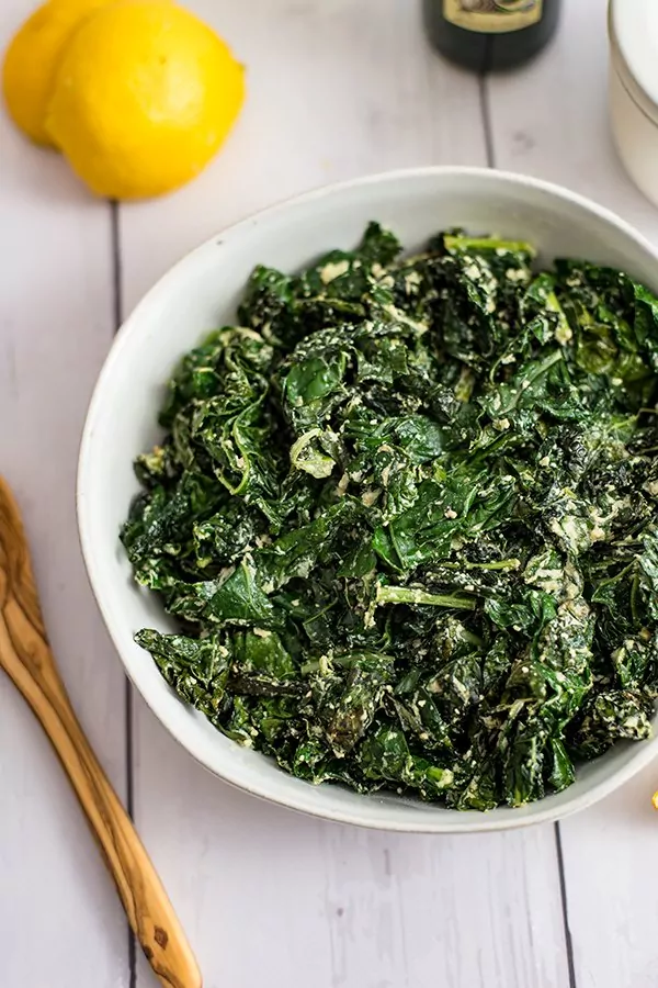 Bowl of creamy kale with a lemon in background and wooden spoon
