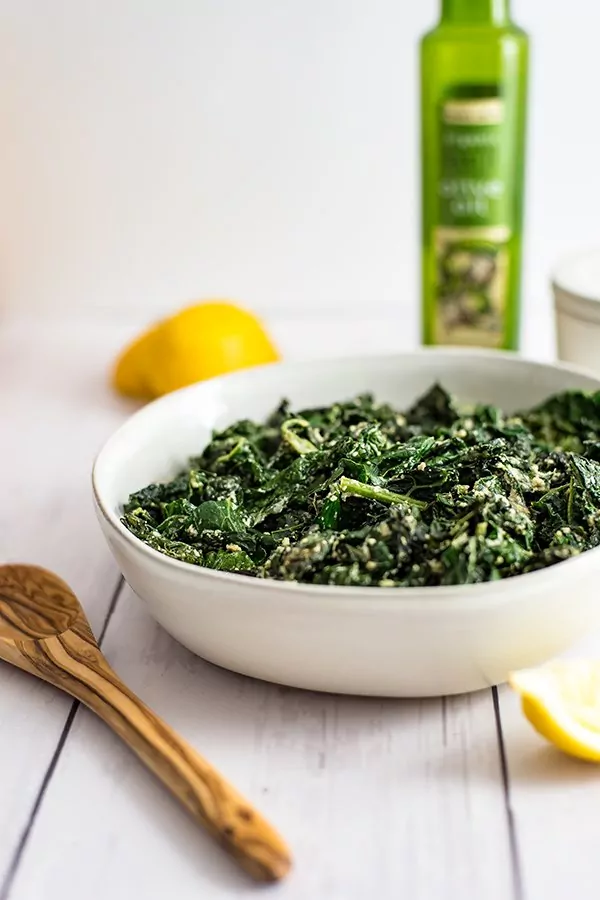 Bowl of creamy kale with a wooden spoon to the side
