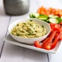 Bowl of roasted cauliflower hummus next to sliced red bell pepper on a white tray