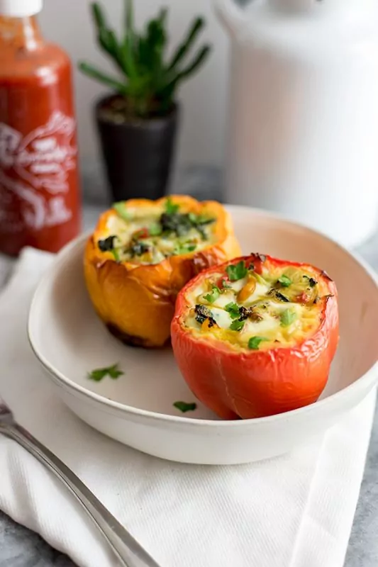 A red and yellow egg stuffed pepper on a white plate with a bottle of sriracha, a succulent and a white pitcher in the background