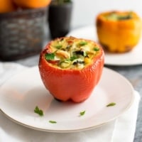 A red egg stuffed pepper on a white plate with an orange pepper in the background