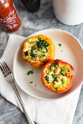 Overhead shot of a red and orange egg stuffed pepper on a white plate with a fork on top of a napkin the left of the plate.