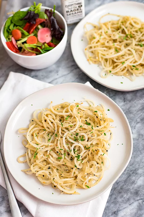 white bowl with low carb pasta made of daikon radish with parsley on top with a salad in a white bowl and a second plate of low carb pasta off to the right in the background