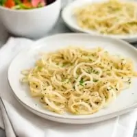 white bowl with low carb pasta made of daikon radish on a white napkin with parsley on top with a salad in a white bowl and a second plate of low carb pasta off to the right in the background